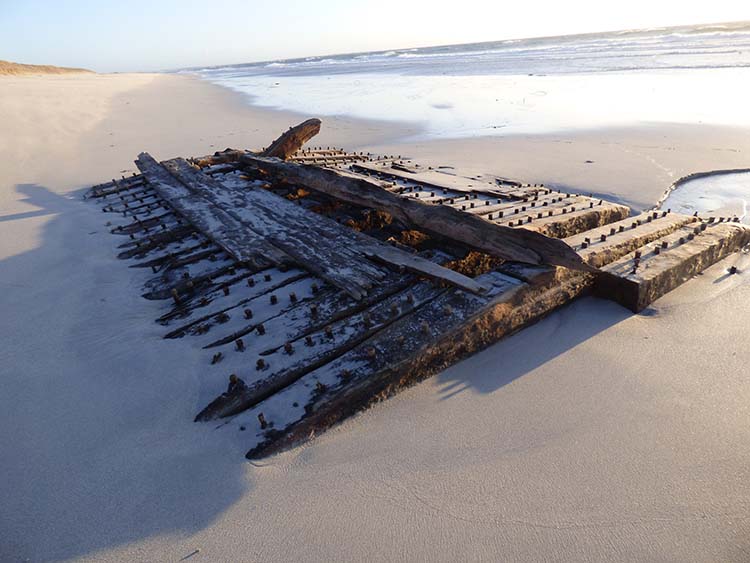 A wooden shipwreck partially buried in sand on a beach