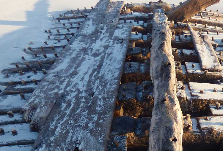 A close up of a wooden shipwreck partially buried in the sand