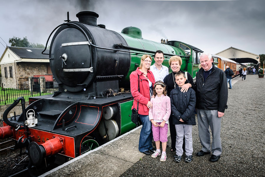 A family group standing in front of a heritage train on a platform