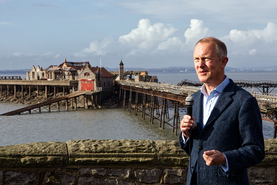 Person stands holding a microphone with pier in the background