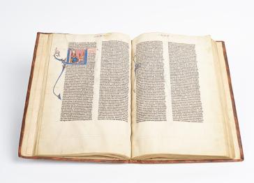 An open book with an elaborately illuminated initial at the top of the lefthand page