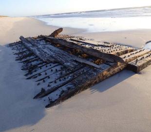 A wooden shipwreck partially buried in sand on a beach